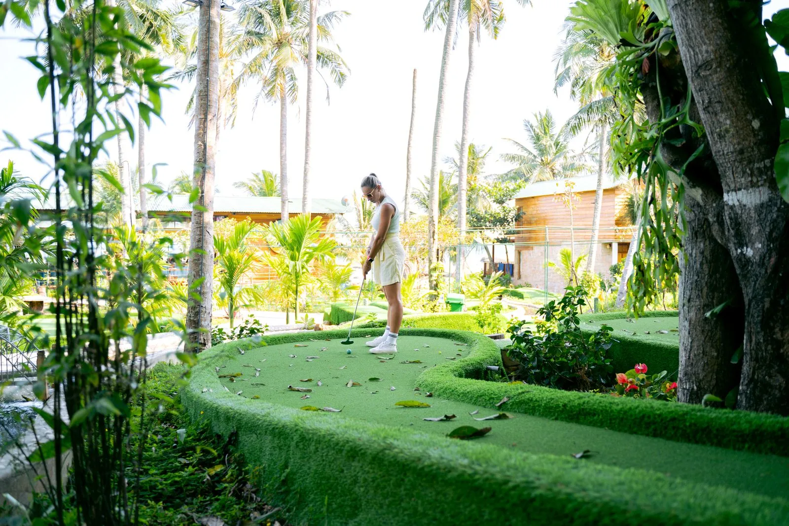 A woman enjoying a game of mini golf in a lush tropical garden with palm trees.